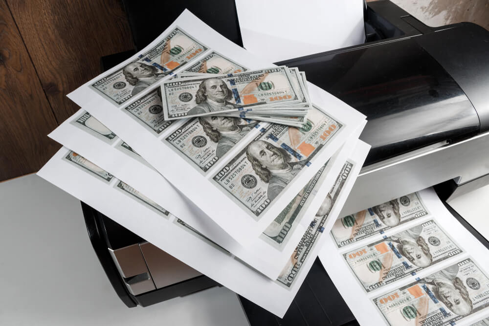 Sheets of counterfeit money sit on top of a printer.
